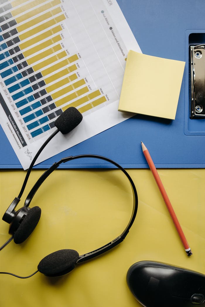 Aerial view of office supplies including graph, headset, pencil, post-it on a colorful desk.